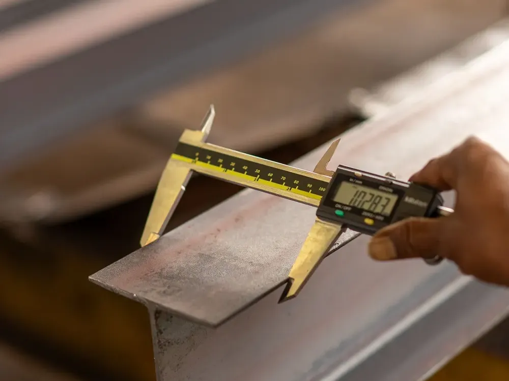 Hand using a digital vernier caliper to precisely measure a steel beam